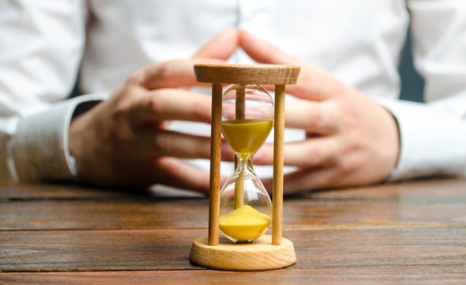 An hourglass and businessman holds his hands in the lock. Job interview concept. Business planning. Management and distribution of time. Making a business deal. Debt restructuring.