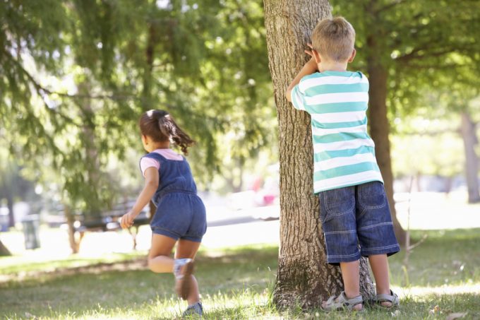 Two Children Playing Hide And Seek In Park