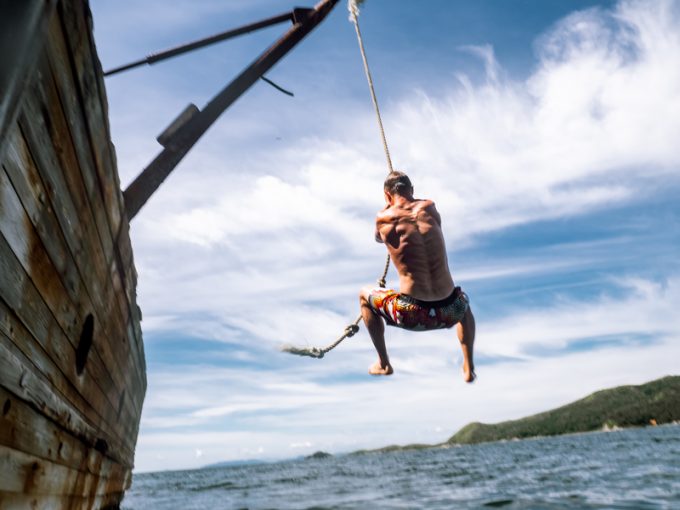 Cliff jumping: A young guy in shorts jumps into seawater from the side of an old ship.