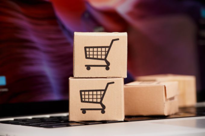 Online shopping . ecommerce and delivery service concept : Paper cartons with a cart or trolley logo on a laptop keyboard, depicts customers order things from retailer sites via the
