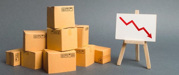 A pile of cardboard boxes and easel with red arrow down. Decrease in the quality, price, quantity and competitiveness of goods and products. Concept drop in industrial production, sales fall.