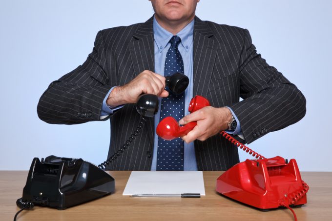 Businessman sat at desk with two telephones.