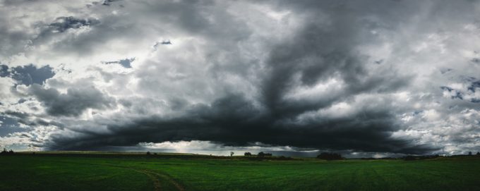 Dark storm clouds panorama above the green grass field