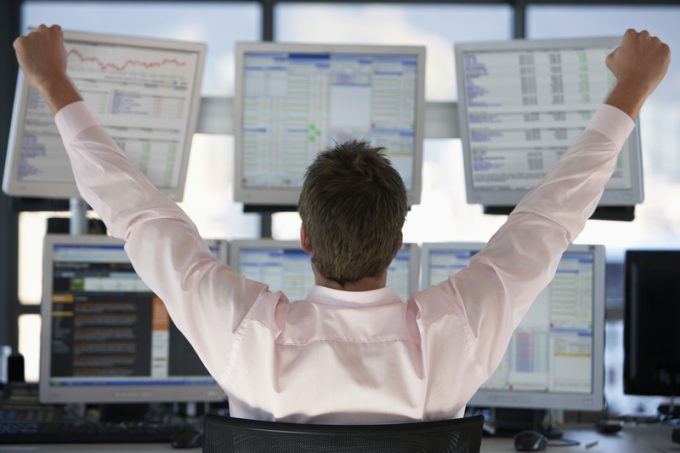 Stock Trader Watching Computer Screens With Hands Raised